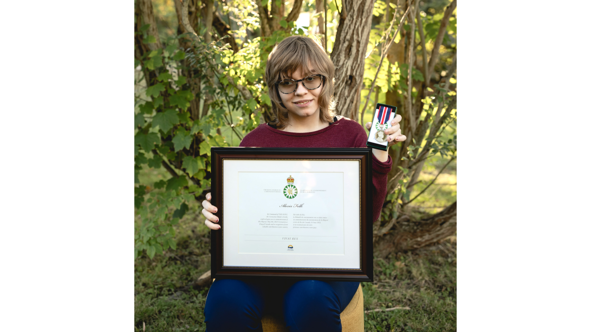 Alexis Folk, 2024 King Charles lll Award Recipient A young woman with wavy blonde hair wearing a burgundy sweater seated on a chair in a forest holding a medal and a framed certificate.
