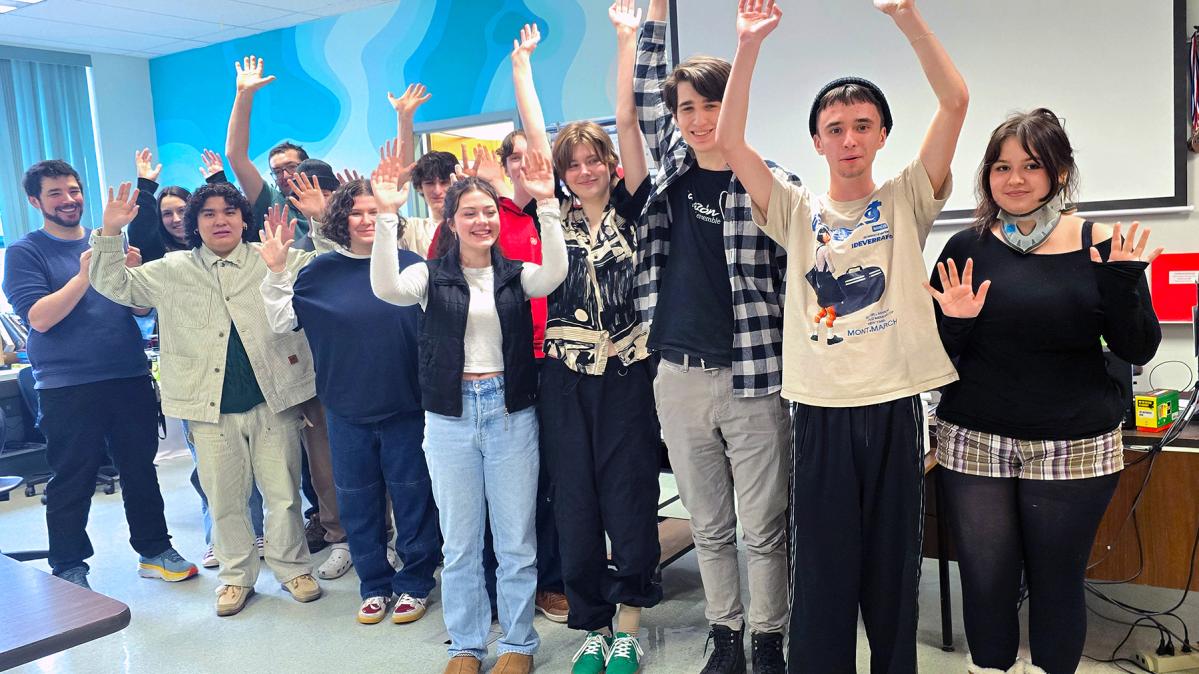 A group of  young people and their teachers with hands raised in celebration in a school classroom