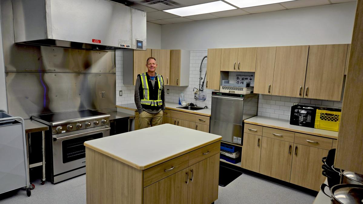 A carpenter wearing a reflective shirt stands in a newly renovated school kitchen.