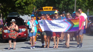 A group of people dressed in bright colours hold a Pride banner