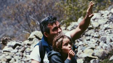 Foster Family Month Man gesturing toward rock face with young child sitting in front of him as if explaining something to the child.