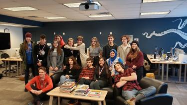 A group of young people in a classroom posting sitting and standing in front of a low table.