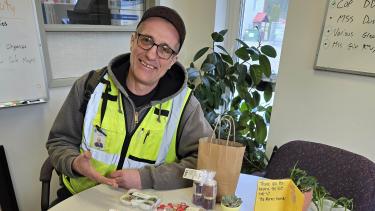 A man in a ball cap, glasses and a flourescent green vest sits at a table covered in hand-drawn cards and messages.