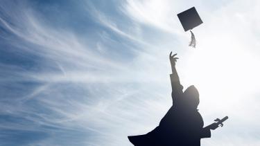Silhouette of a person in a graduation gown holding a diploma and throwing their tassled hat in the air against a blue, cloud painted sky.