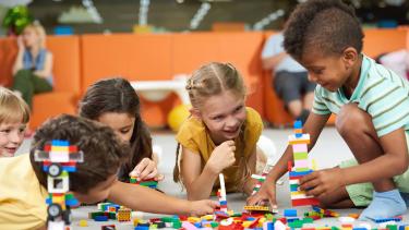 A group of young children play with lego on the floor in a play area.