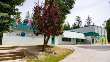 A white, stucco flat-roofed elementary school with green trim behind some trees