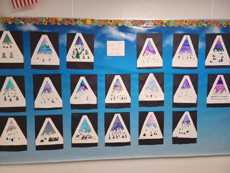 A series of mountain-shaped white triangles on top of black rectangles pasted in turn on a sky blue sheet of paper, in turn mounted on a white wall.