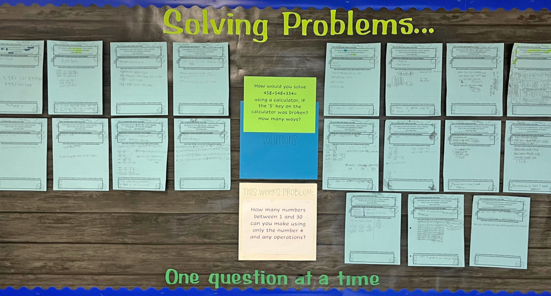 A brown wooden plank wall with sheets of paper attached to it showing solutions to a math problem