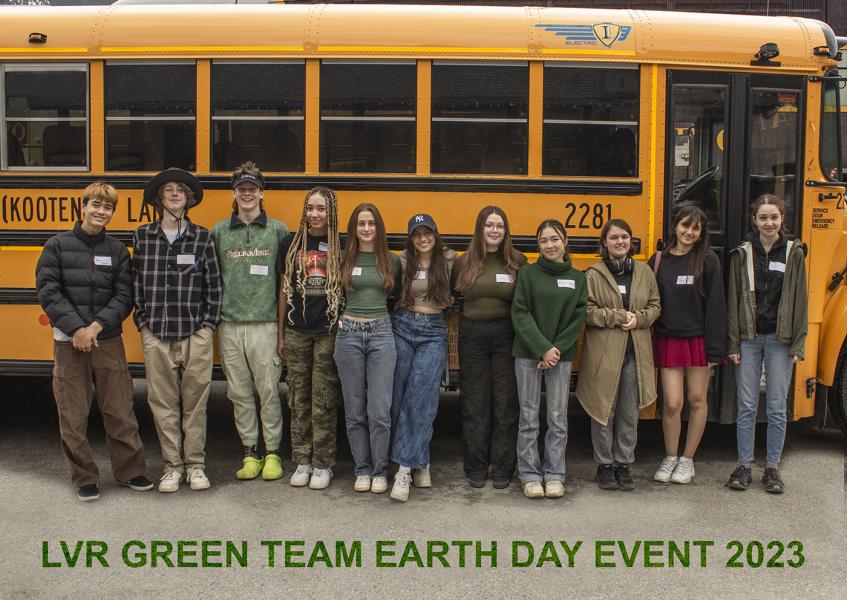 Smiling, casually dressed high school students pose with their backs against the side of a school bus.