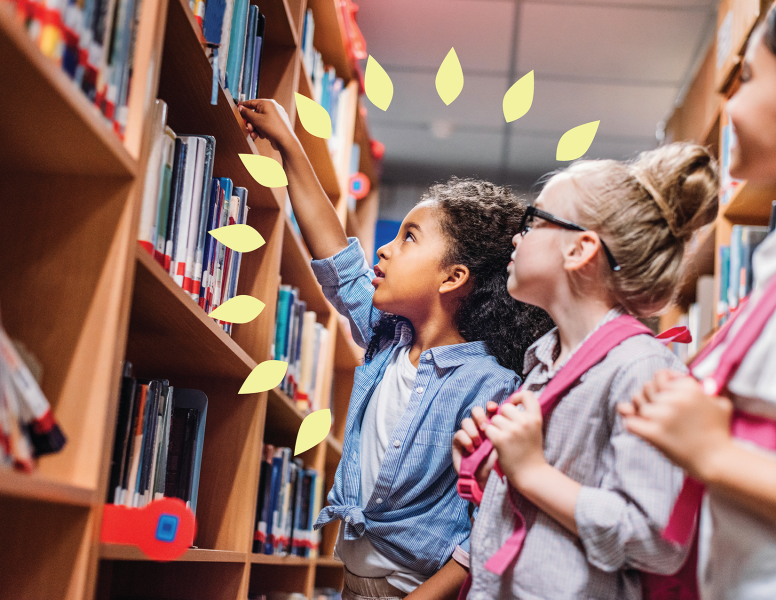 Three grade-school girls in library corridor seen from sideview, with first girl reaching for a book from the shelf. 