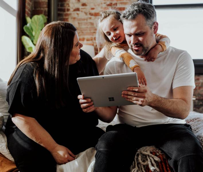 A woman, man and child look at a laptop inside a bricked-walled apartment