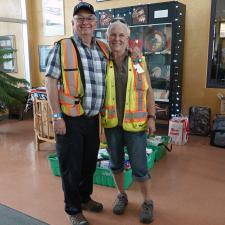 Man and woman in reflective vests stand arm in arm