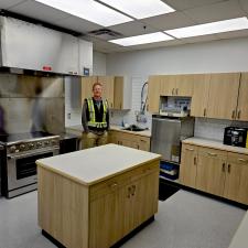 A carpenter wearing a reflective shirt stands in a newly renovated school kitchen.
