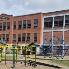 A rectangular brick school building with a playground in front.