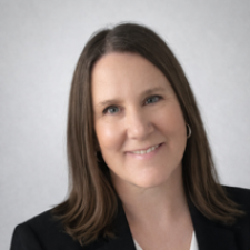 A woman with shoulder-length brown hair wearing a black blazer and white button-up shirt.